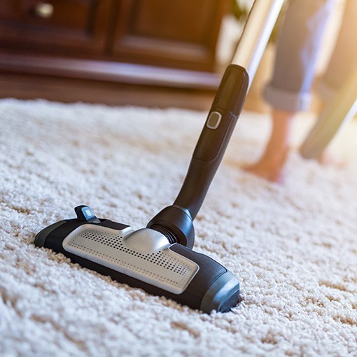 Young woman using a vacuum cleaner while cleaning carpet in the house.